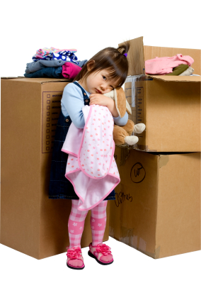 Small child standing in from of packed boxes of toys and clothes.